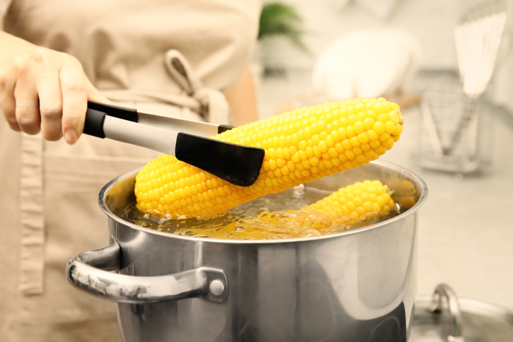 Woman,Taking,Boiled,Corn,From,Pot,With,Tongs,In,Kitchen,