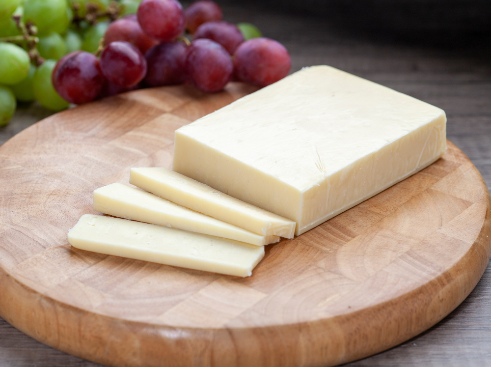 Mild,White,Cheddar,On,Wooden,Board,With,Grapes
