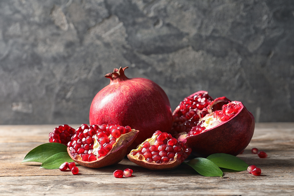 Ripe pomegranates and leaves on table against grey background. Space for text