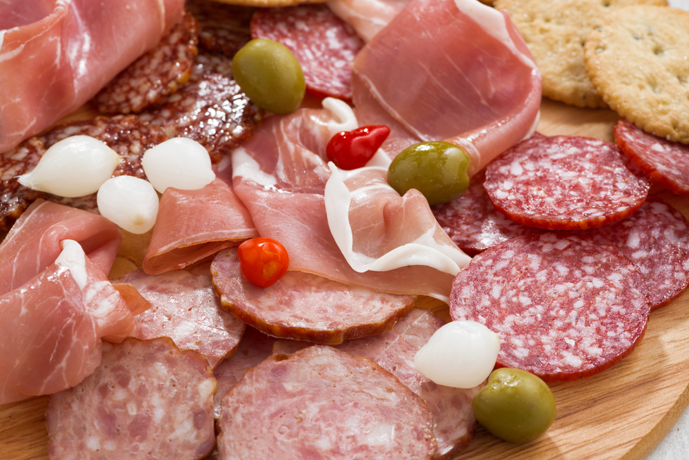 Assorted deli meat snacks, sausages and pickles on board, close-