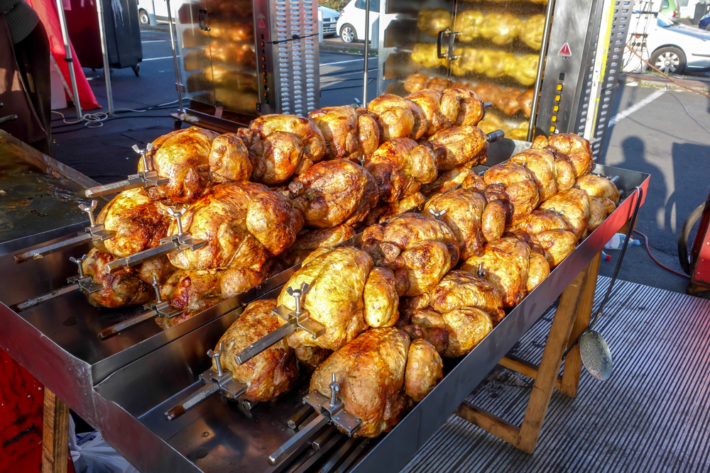 Roasted chicken on large rotisseries with rotating spit for roasting and barbecuing meat at the outdoor sunday market